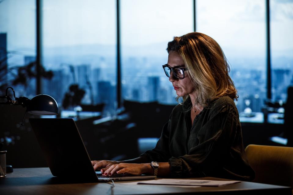 Portrait of serious businesswoman in eyeglasses using laptop at her desk