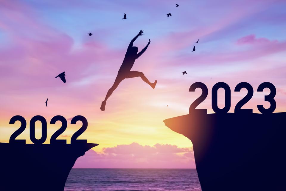 Hombre silueta saltando entre acantilados con el número 2022 a 2023 y pájaros volando en la cima de la montaña. Desafío de la libertad y concepto de vacaciones de aventura de viaje.