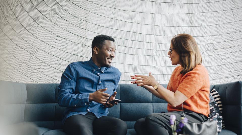 Businessman and woman using mobile phones while sitting on couch during conference