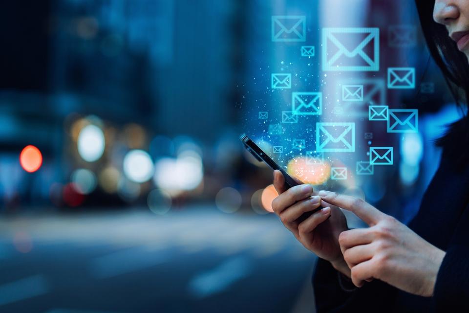 Primer plano de una joven asiática que envía un correo electrónico con un smartphone en la ciudad, contra las luces de las calles de la ciudad iluminadas en el distrito del centro. concepto de tecnología de la información