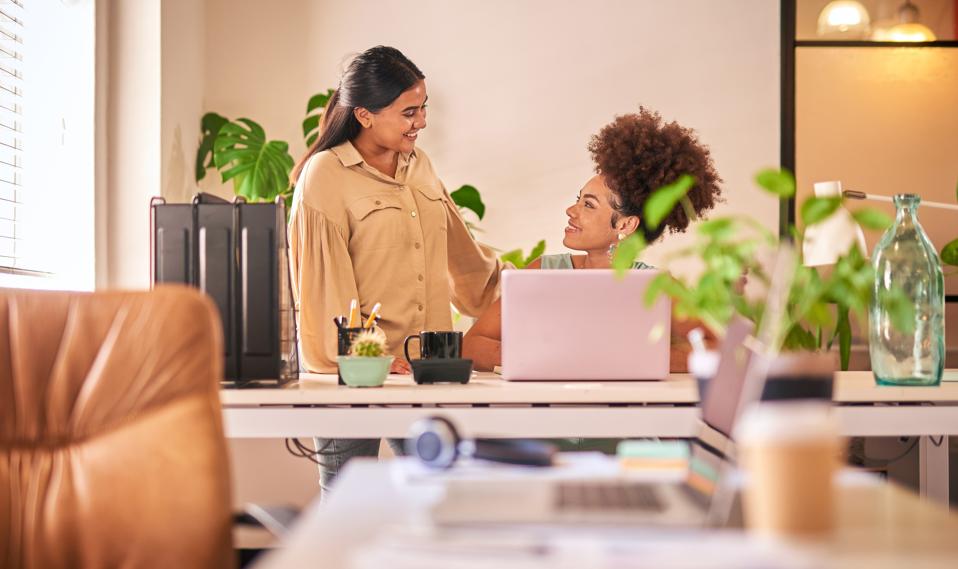 Dos empresarias de raza mixta charlando en un escritorio. Joven empresaria india discutiendo ideas de diseño con una colega africana. Encuentro para innovar y desarrollar la empresa