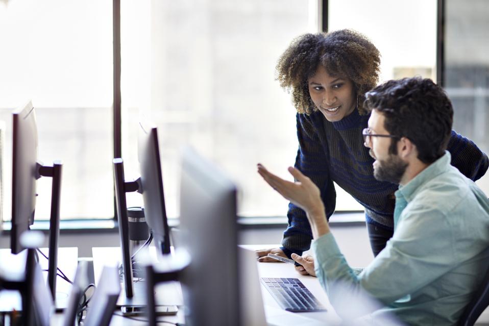 Business people discussing over desktop computer at desk against window in office