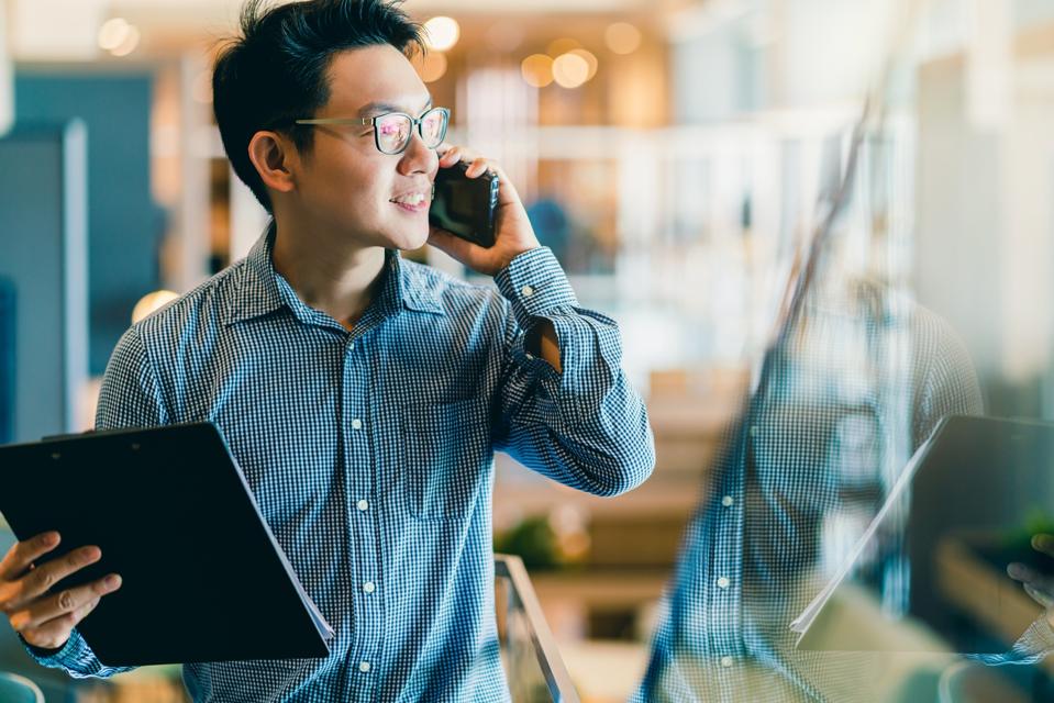 confianza inteligente empresario de inicio asiático propietario de la empresa empresario sonrisa uso de la mano teléfono inteligente trabajando en el fondo de la oficina