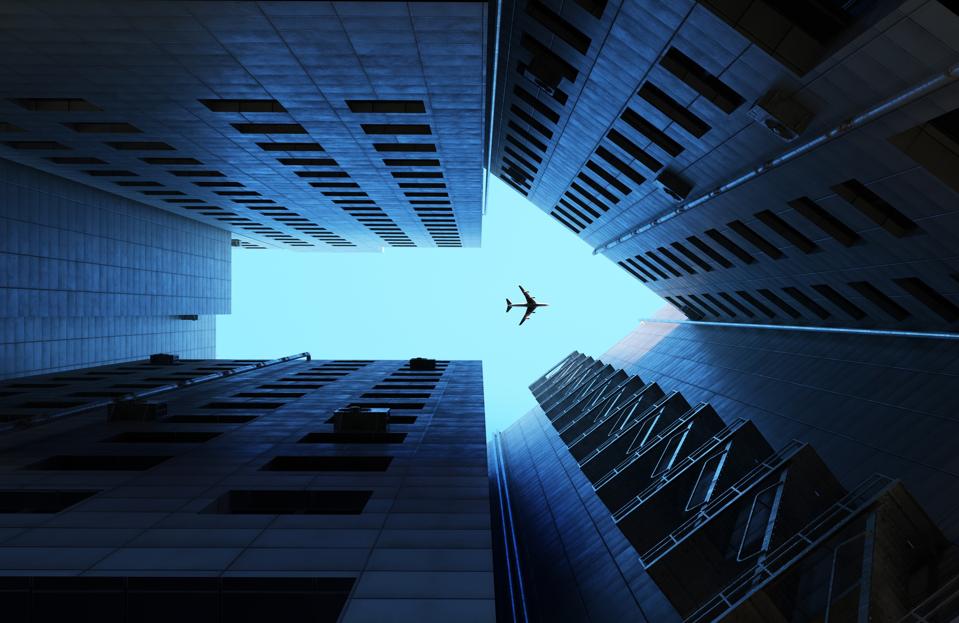 Image of buildings making arrow sign with airplane flying on blue sky.