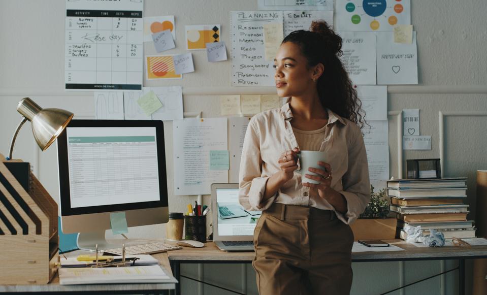 Businesswoman standing and looking contemplative while holding a cup of coffee in her home office