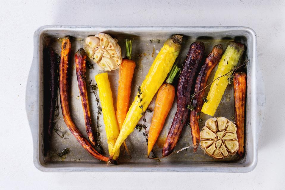 Baked whole colorful carrots with garlic and thyme in vintage aluminum tray over old wooden surface. Top view