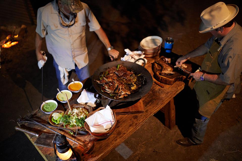 Two men cooking next to an open fire