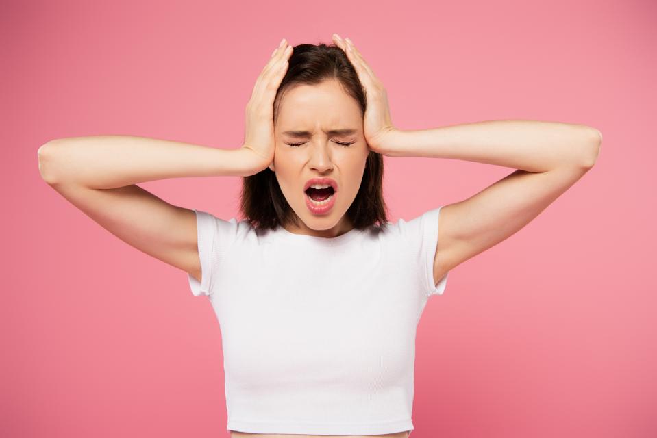 Woman with hands on head and closed eyes screaming isolated on pink