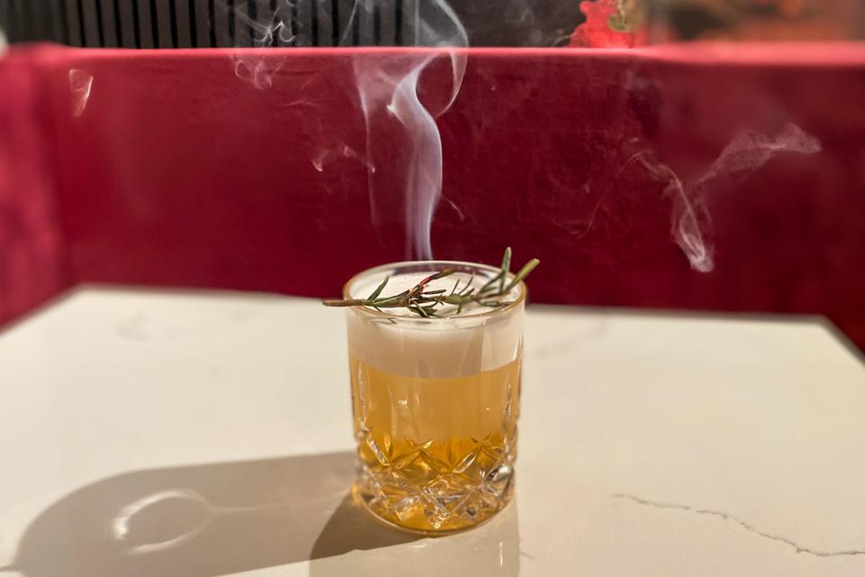 A cocktail with a smoking rosemary branch