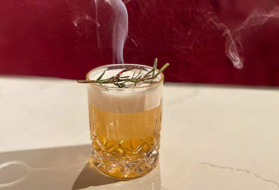 A cocktail with a smoking rosemary branch