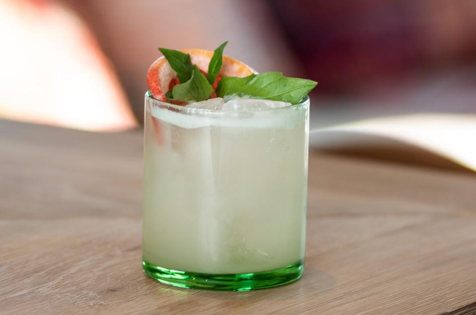 A cocktail in a glass garnished with grapefruit and basil.