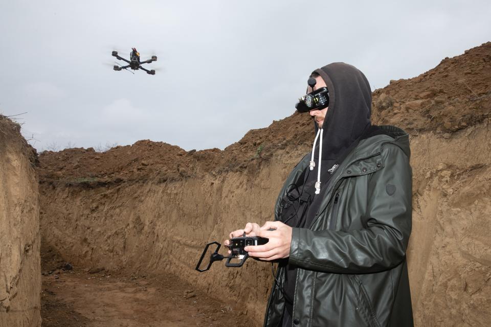 A drone operator wearing FPV glasses is seen in a trench...