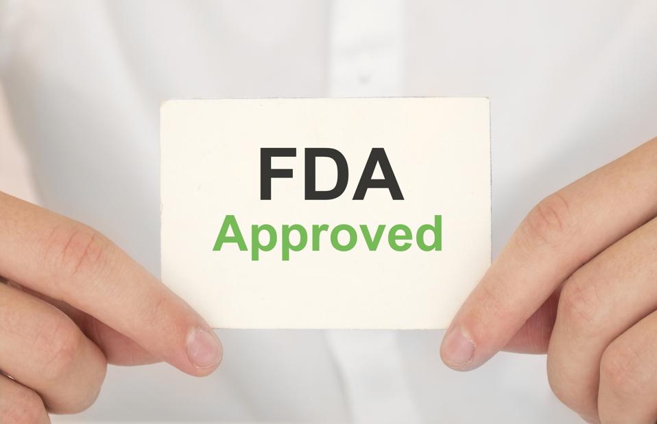 Hand holding a paper FDA APPROVED on green background