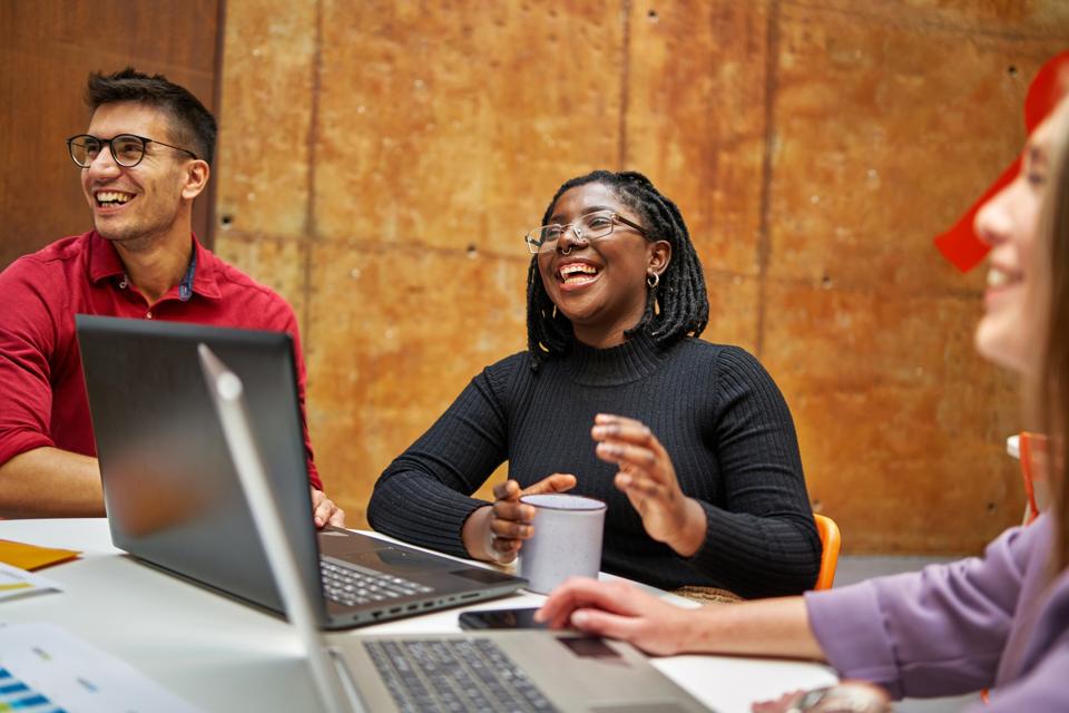 Young modern businesswoman in coworking space laughing with her colleagues while working