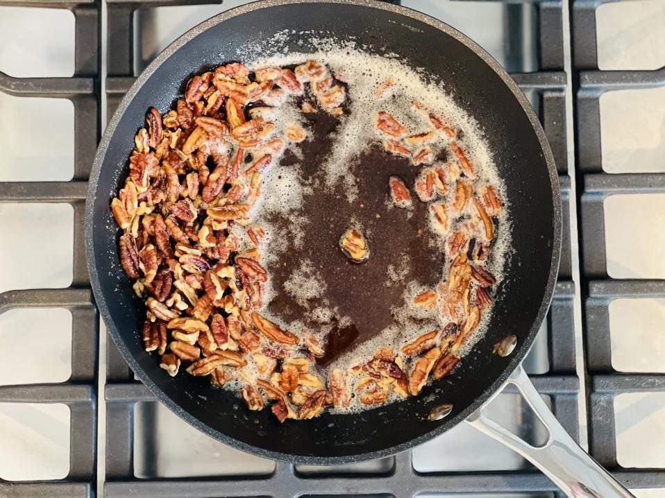A skillet of cooled nutty brown butter and pecans is seen on top of a gas burner.