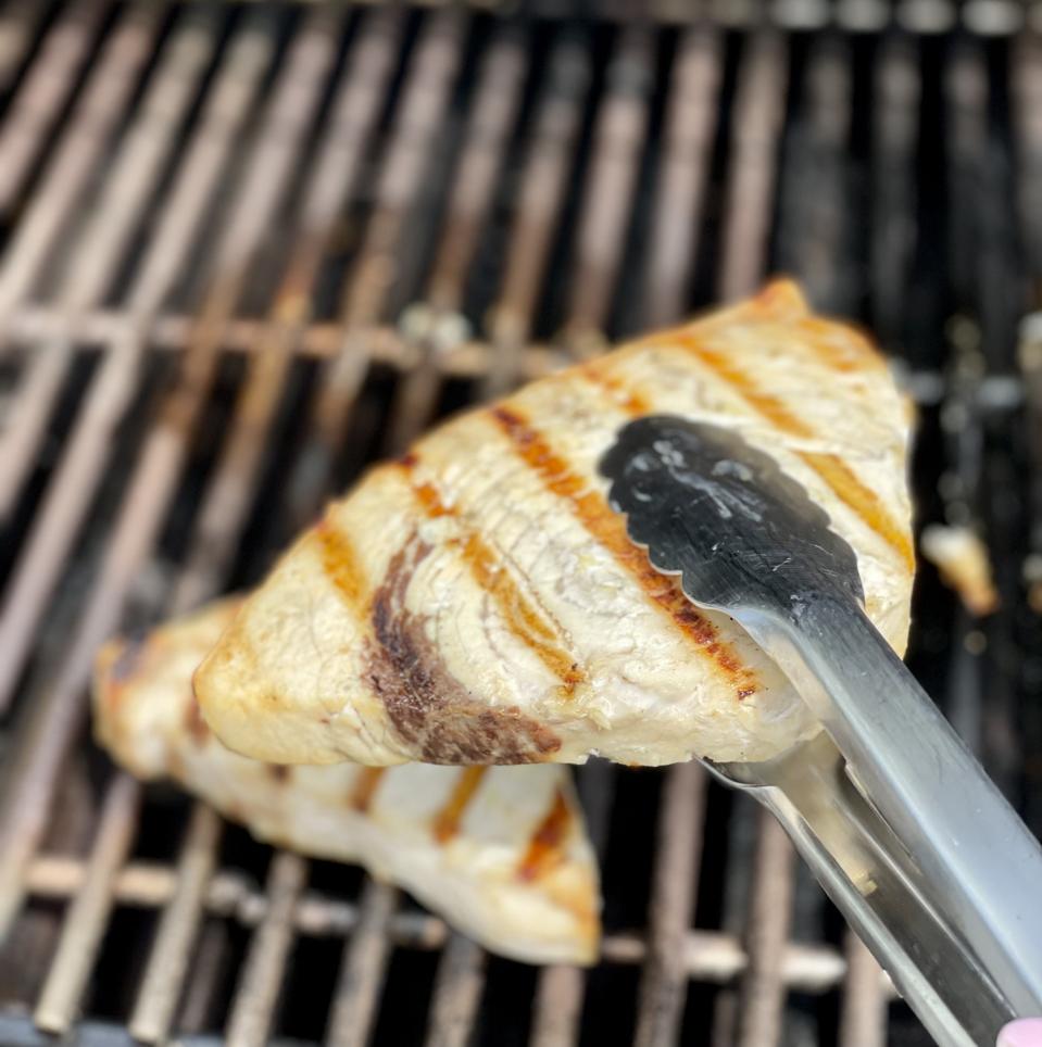 A pair of tongs picks up a grilled swordfish steak from a hot cooking grate. Grilled fish doesn't stick if you coat the fish with olive oil, wait until it is fully cooked, and make sure the cooking grates are very clean.