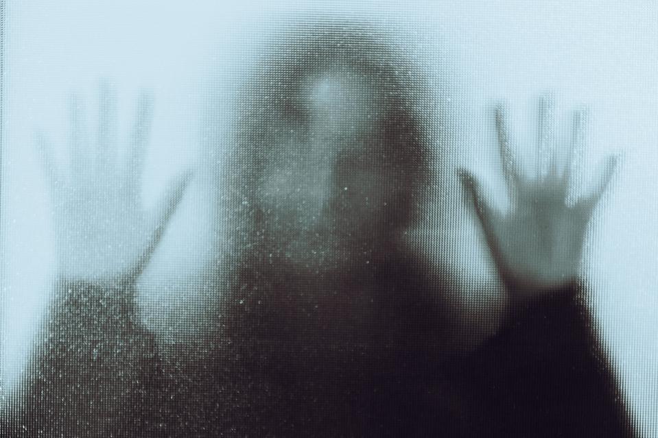 A desperate woman pressing her hands up against a glass window