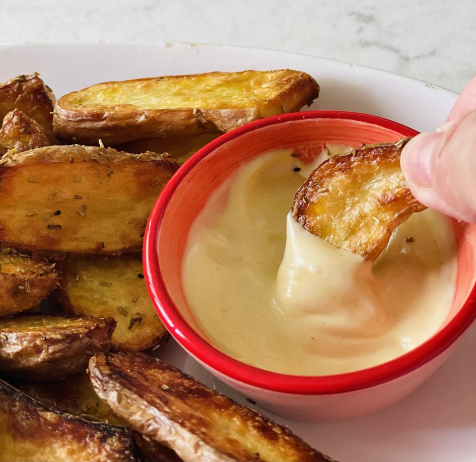A hand is shown dipping crispy potatoes in Aioli in this photograph by Elizabeth Karmel. Potatoes aren’t just for dinner anymore, serve them with a dipping sauce as a nibble with drinks—no one will miss the cheese and crackers!