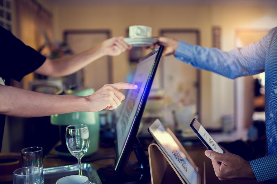 Selective focus to tablet and blurry customer using smart phone scan QR code on tablet to payment with cashier machine at counter bar in coffee shop.