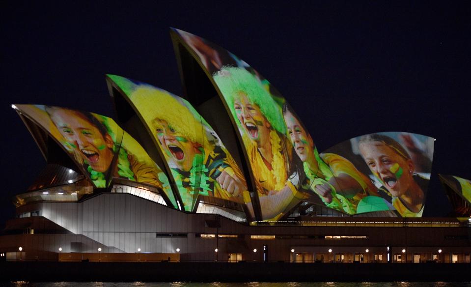 Sydney Opera house lit up with faces of young Australian soccer fans.