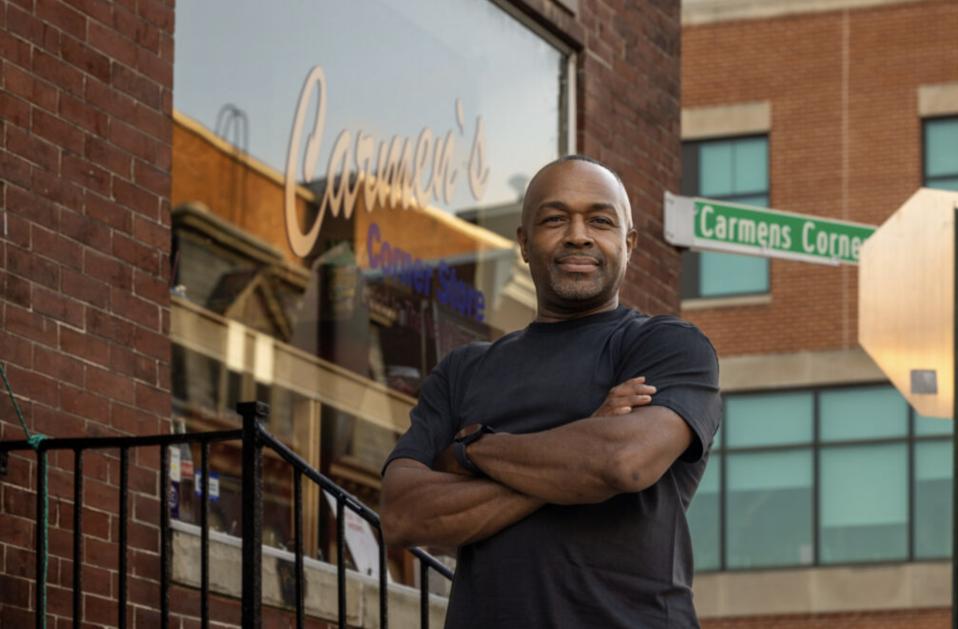 man stands with arms crossed in front of small store