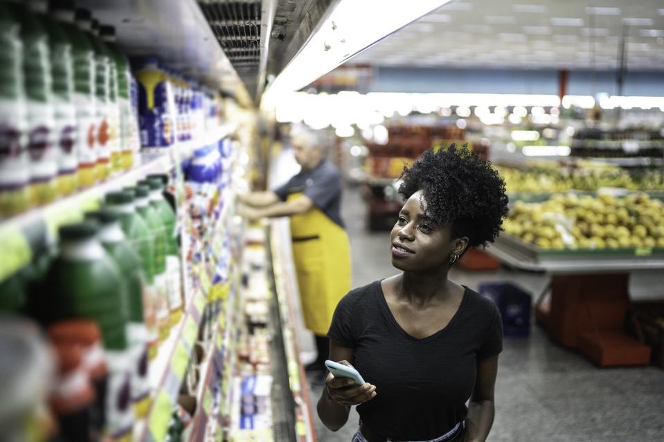 Young woman using mobile phone and choosing product in supermarket