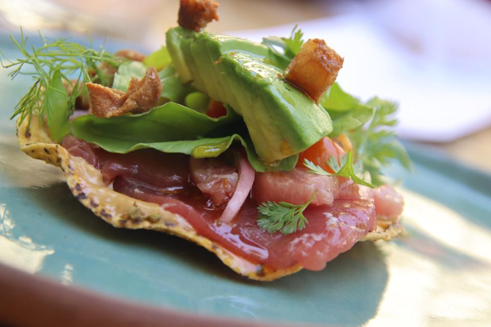 tostada topped with tuna, avocado, and herbs