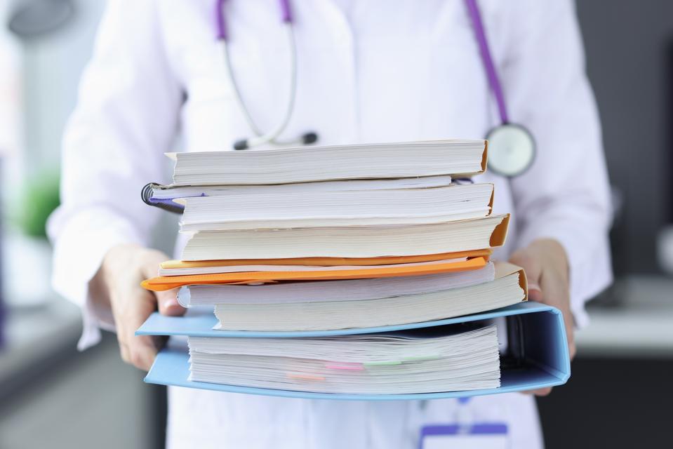 Doctor is holding large stack of folders