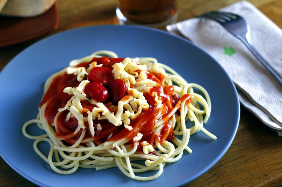 Freshly cooked spaghetti pasta with tomato sauce topped with cheese and hotdog