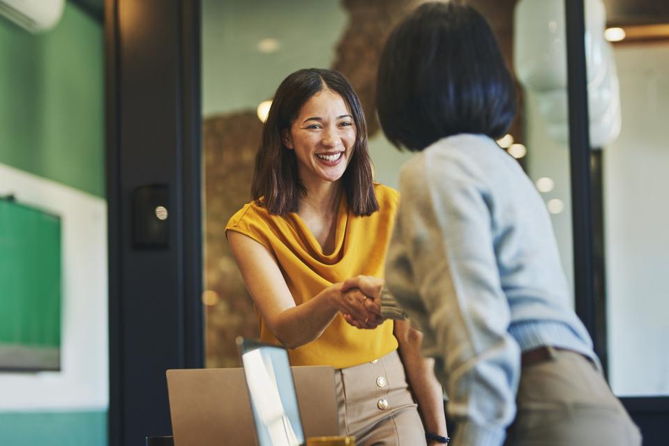 Businesswoman shaking hands with client and smiling cheerfully in meeting room.