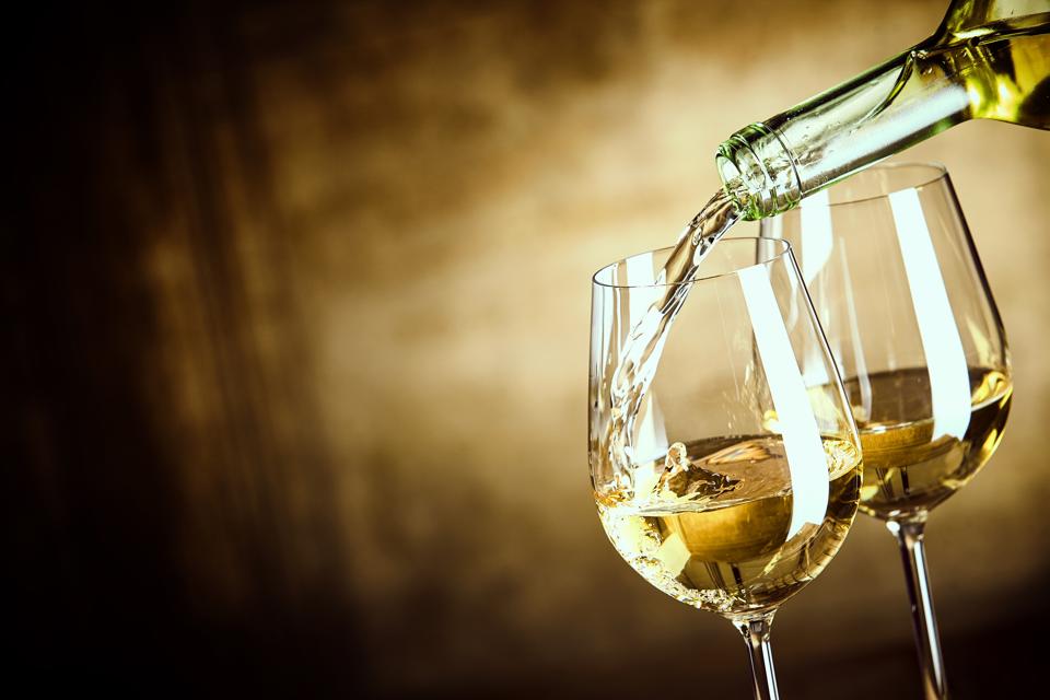 Pouring two glasses of white wine from a bottle in a close up view of the wineglasses.