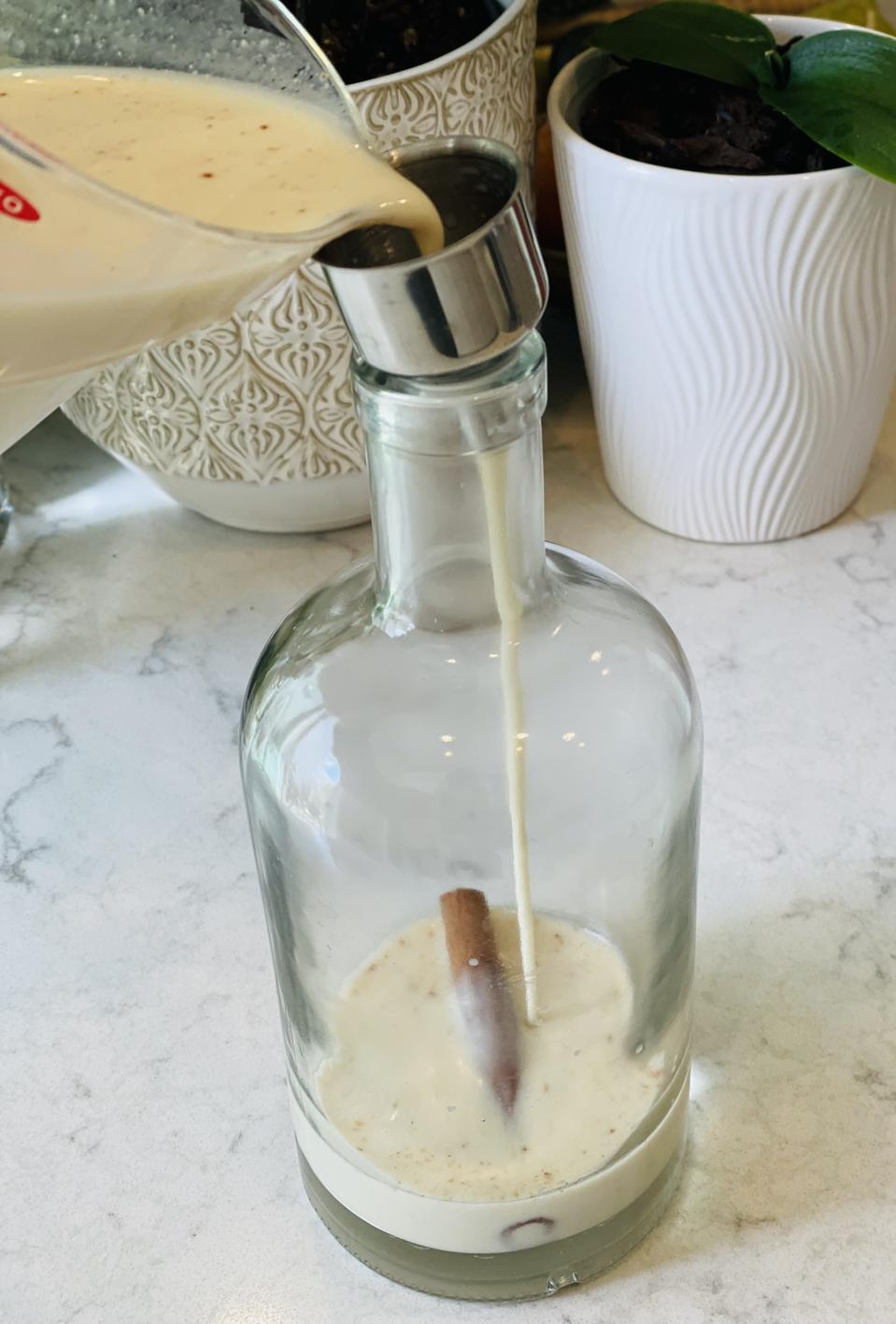 Homemade Caribbean Coquito poured into recycled bottles is an unexpected and welcome holiday gift. In this photograph by Elizabeth Karmel, the author is pouring Coquito into a recycled liquor bottle.