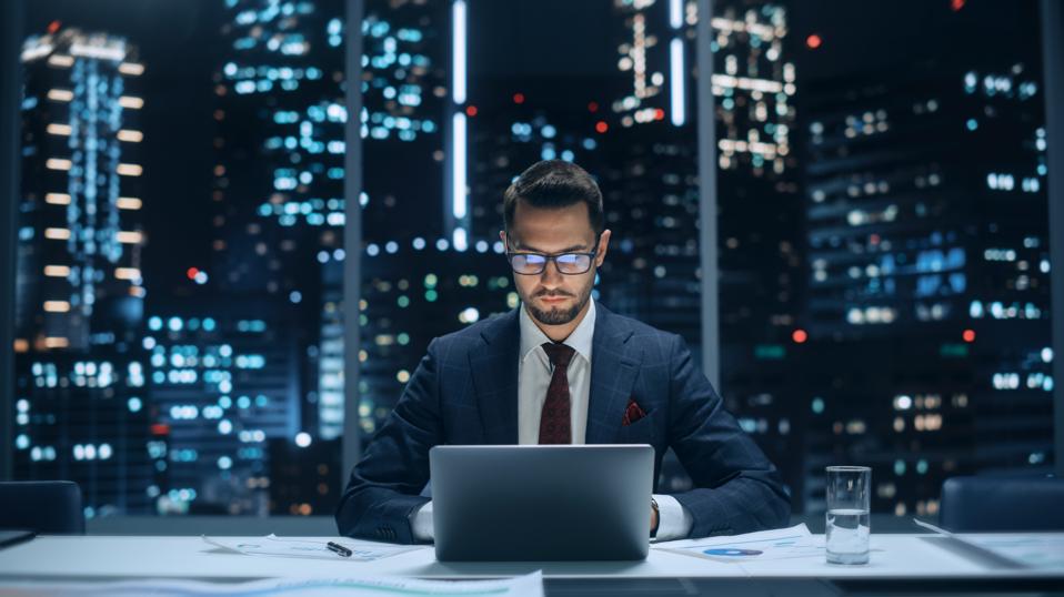 Portrait of a Successful Handsome Businessman Working on Laptop Computer in Big City Office Late in the Evening. Finance Investment Analyst Checking Line and Pie Graphs from Project Management Report.