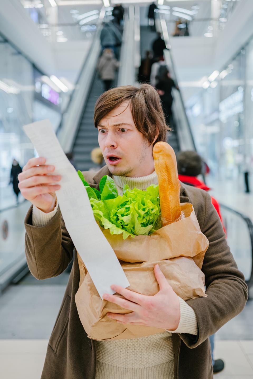 Man unpleasantly shocked by high food prices while looking at paper check in store
