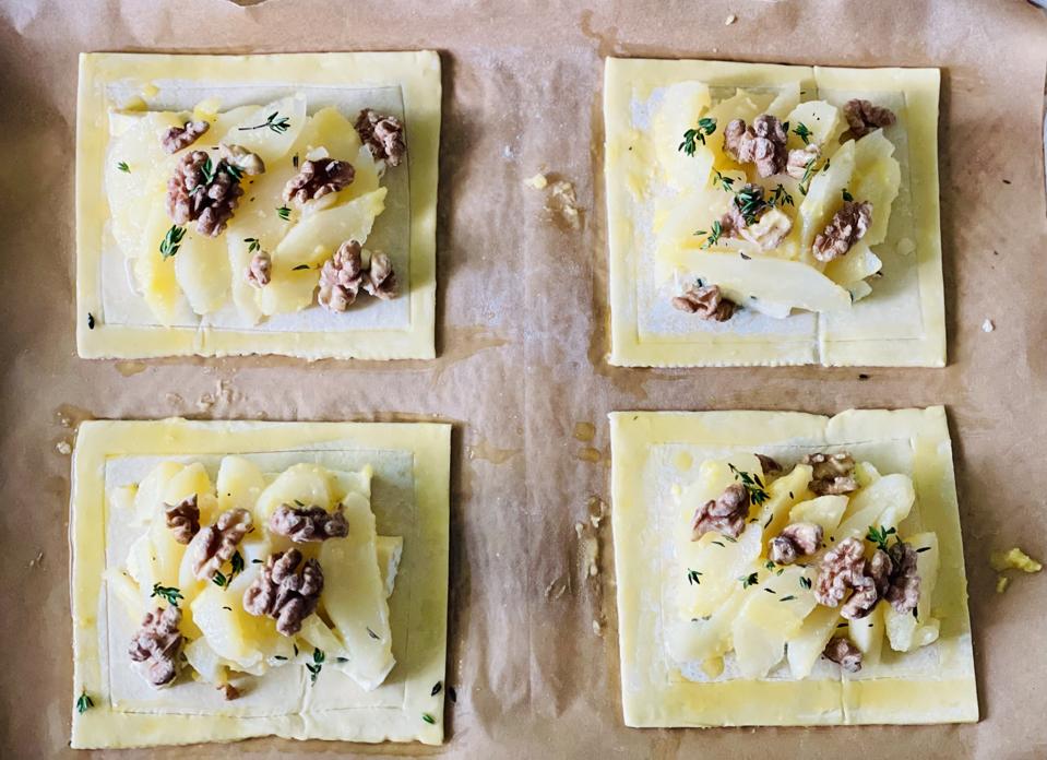 The tarts are filled—inside the lines—and ready for the oven. A tray of Raw tarts is photographed by the author and shows uncooked puff pastry, Blue cheese, pears and walnuts.
