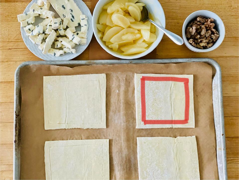 To "score" the pastry, draw a line a half-inch in from the ends with the tip of a paring knife to make a “frame” along the border. The red box in the photo outlines the scoring. In the photograph by the author is an example of the uncooked pastry that has been scored with the tart ingredients of Fromager d'Affinois Bleu cheese, pears tossed in melted butter and walnuts.