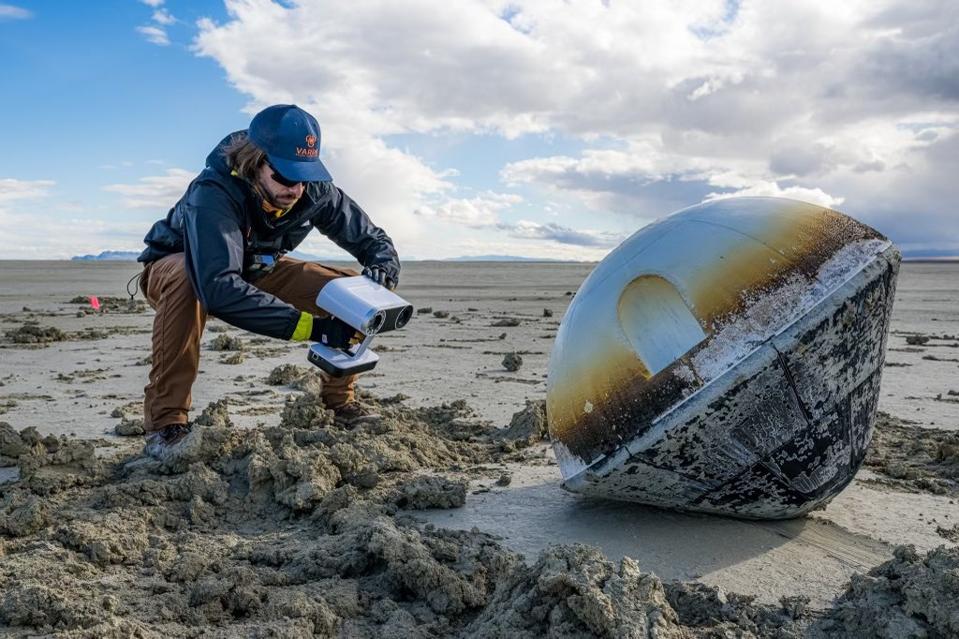 A man on a beach next to a small, mini-fridge sized spacecraft.