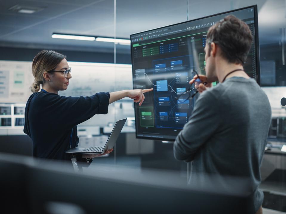 Two Diverse Software Developers Having a Meeting in a Conference Room. Female and Male Tech Industry Engineers Brainstorming Ideas for Their Neural Network Blockchain Startup