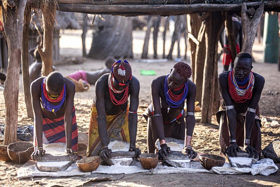 ladies from the Karo tribe in Ethiopia working together with stone grinders to prepare rice grain paste.