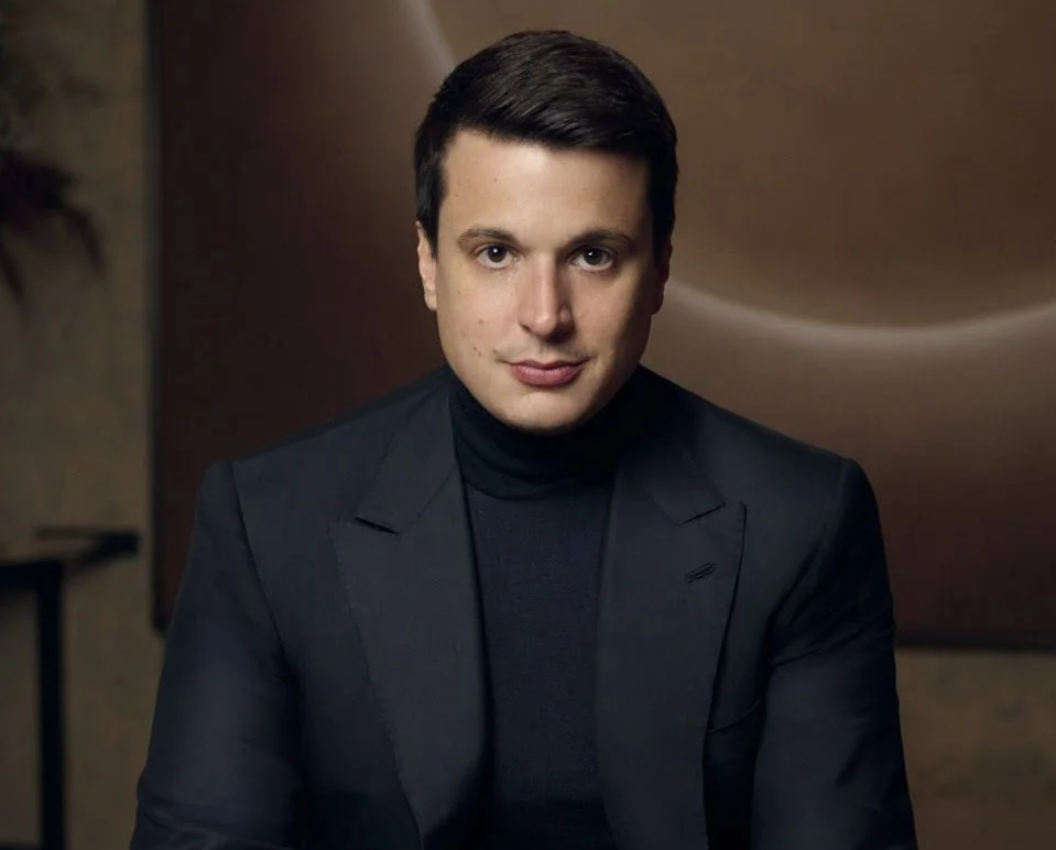 Max-Hervé George wears a dark turtleneck sweater under a dark blazer.