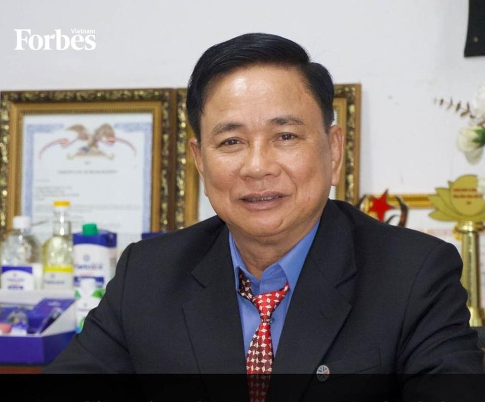 Cu Van Thanh wears a dark jacket, sitting in front of various of his company's products.