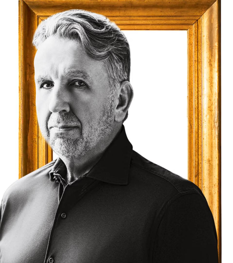 Michał Sołowow wears a dark colored shirt in front of a gold frame.
