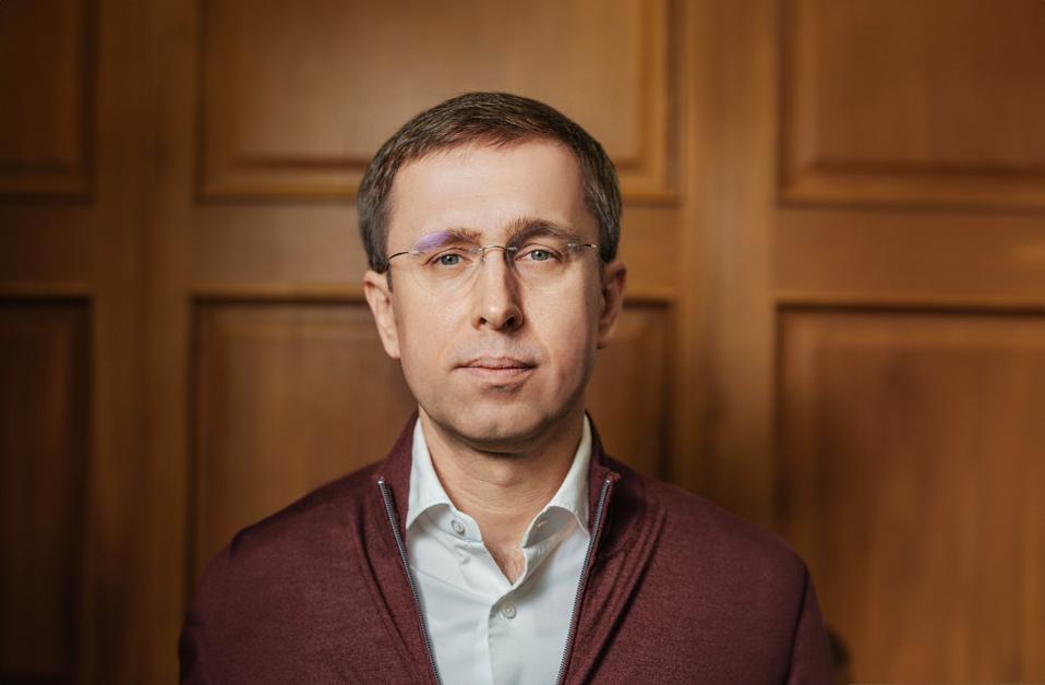 Sergii Koretskyi wears glasses and a white collared shirt against a wood-paneled wall.