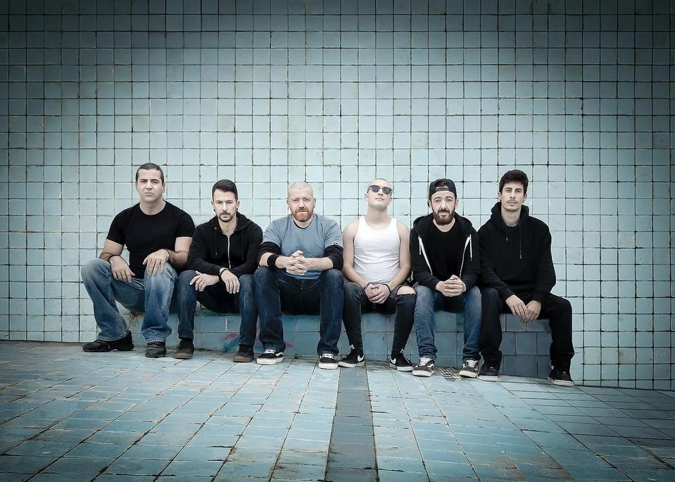 Hybrid Theory band members sit on a bench against a tiled wall.