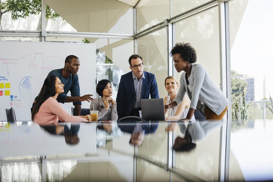 Young businesswoman discussing over laptop with male and female colleagues in meeting room