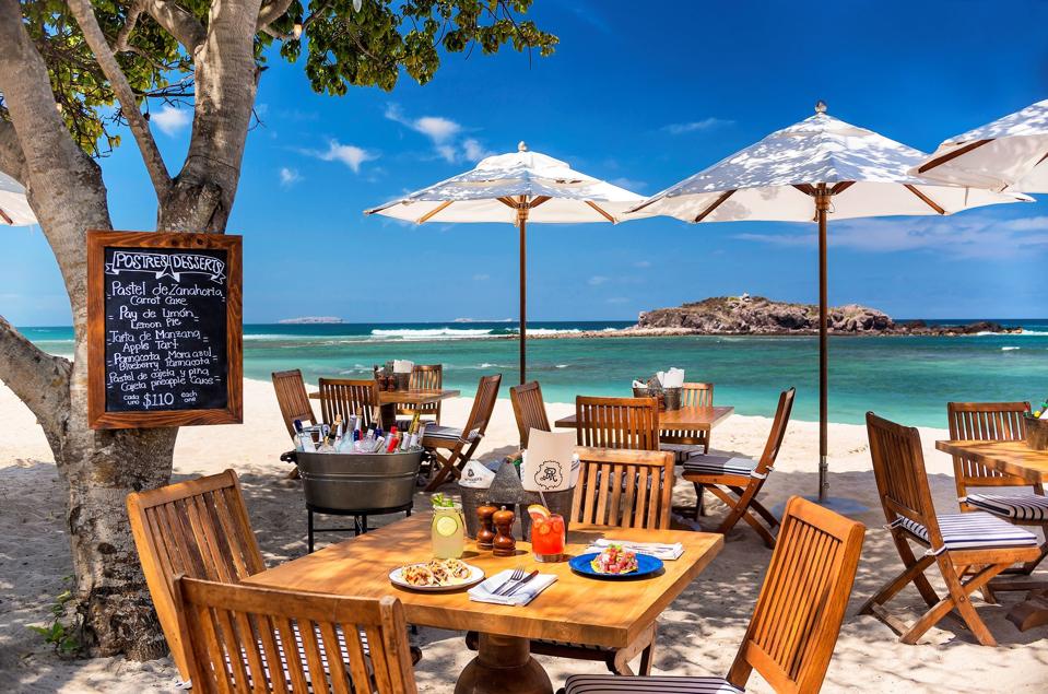 a beach restaurant with tables and chairs and the sea in the background