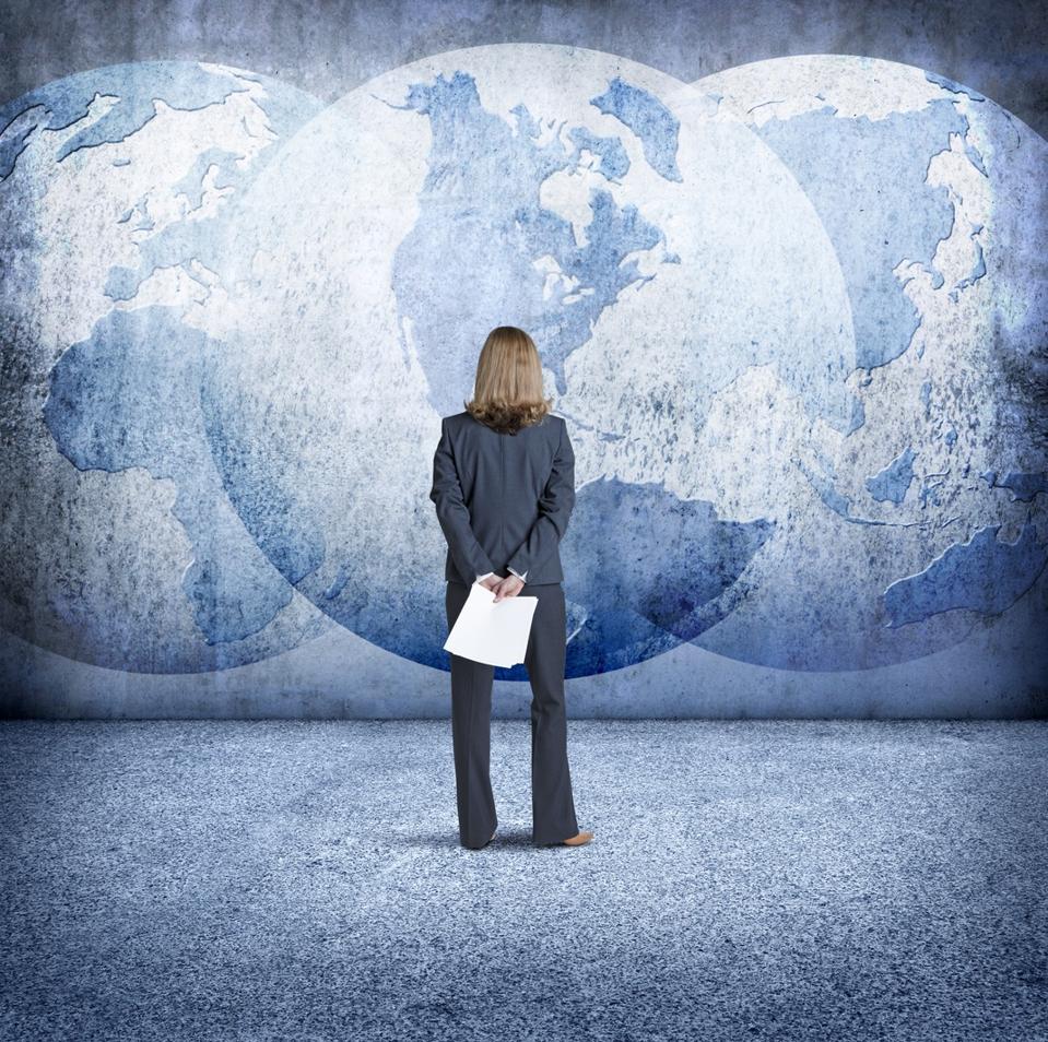 Businesswoman Looks Up At Three Interlocking Globes On Wall