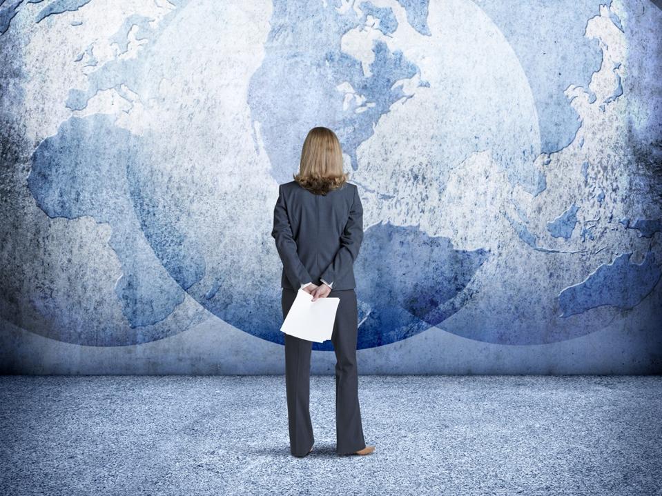 Businesswoman Looks Up At Three Interlocking Globes On Wall
