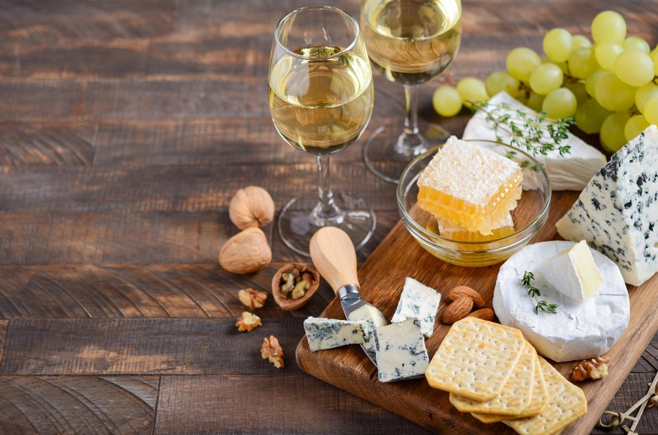 Cheese plate with grapes, crackers, honey, and nuts on a wooden table.
