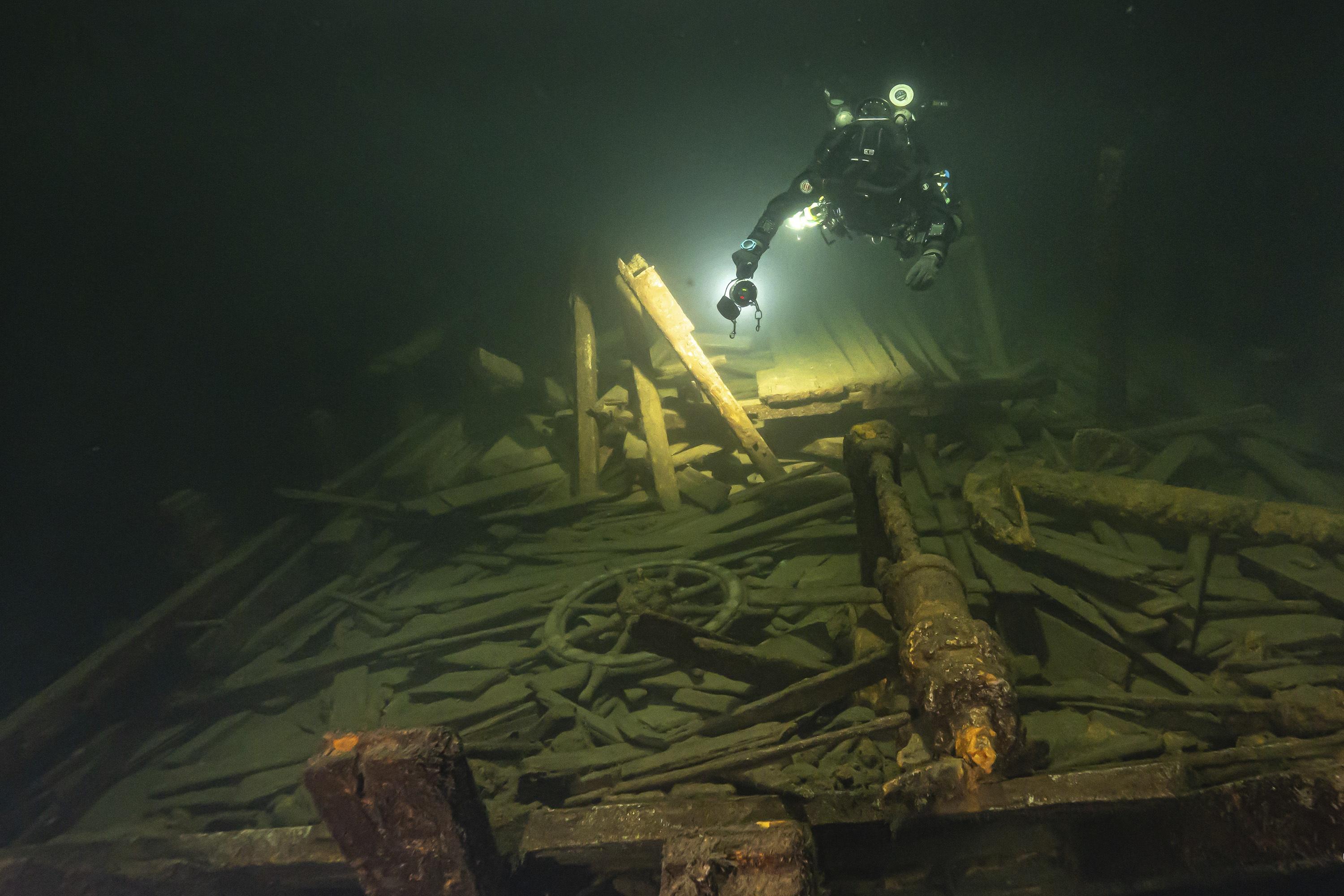 A diver uses a light to inspect wreckage of a 19th century sailing ship.